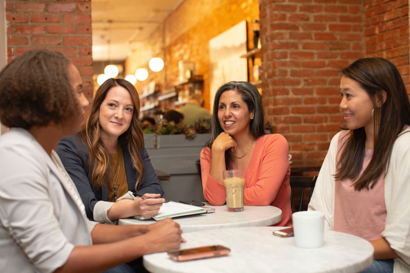 Four professional women talking together around a cafe table