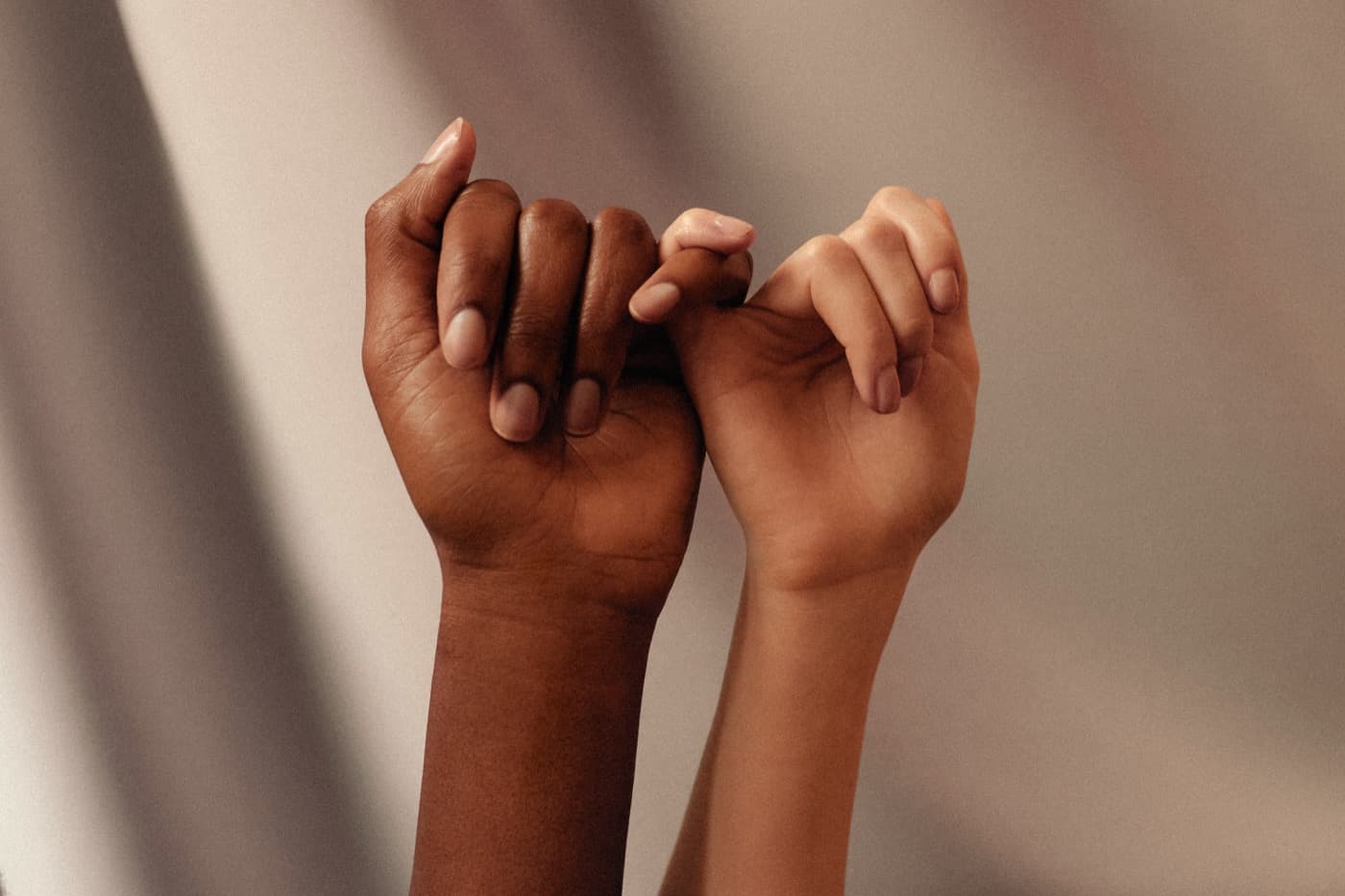 Two hands of different skin tones linking pinky fingers